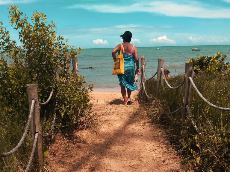 Woman with a beach bag walking on the sand.