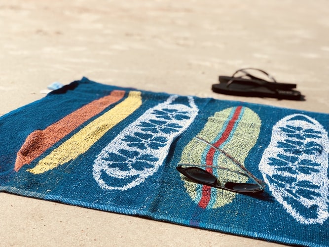 Blue beach towel on sand with sunglasses and flip flops in background