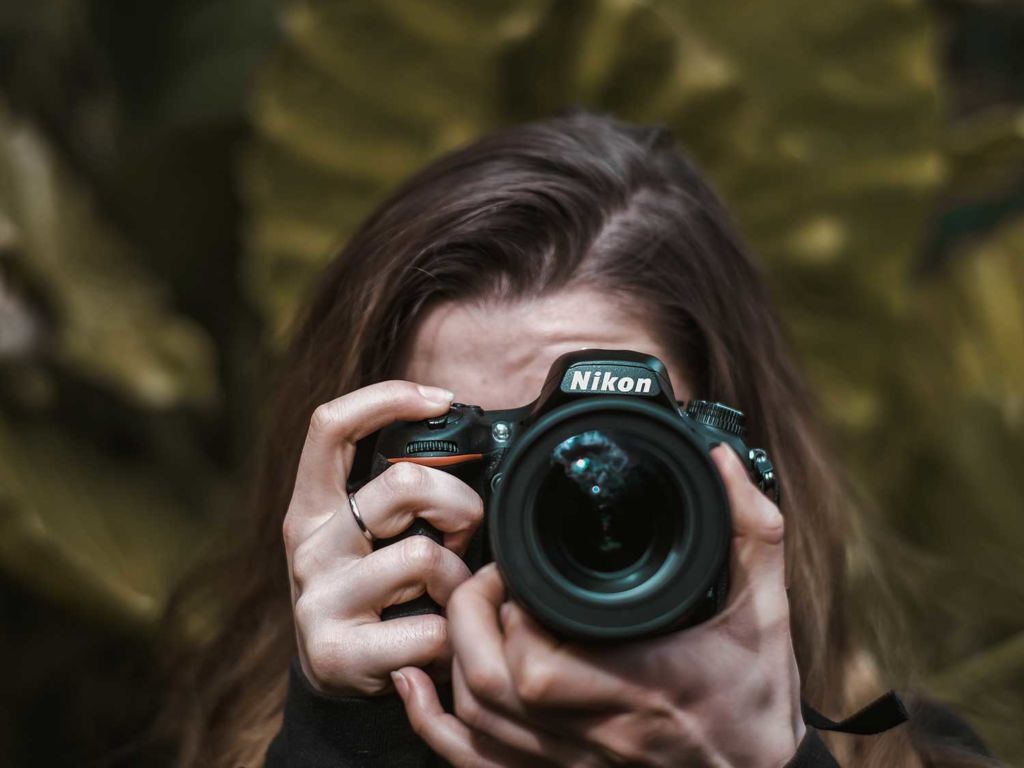 Woman taking pictures in forest with Nikon camera.