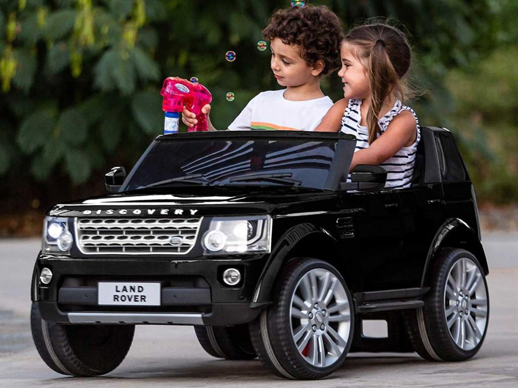 Two kids riding in a toy Land Rover.