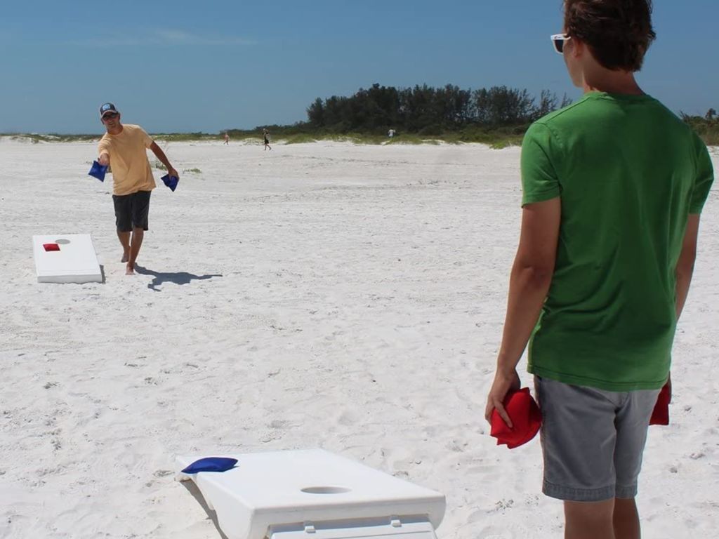 Two guys playing cornhole on a beach