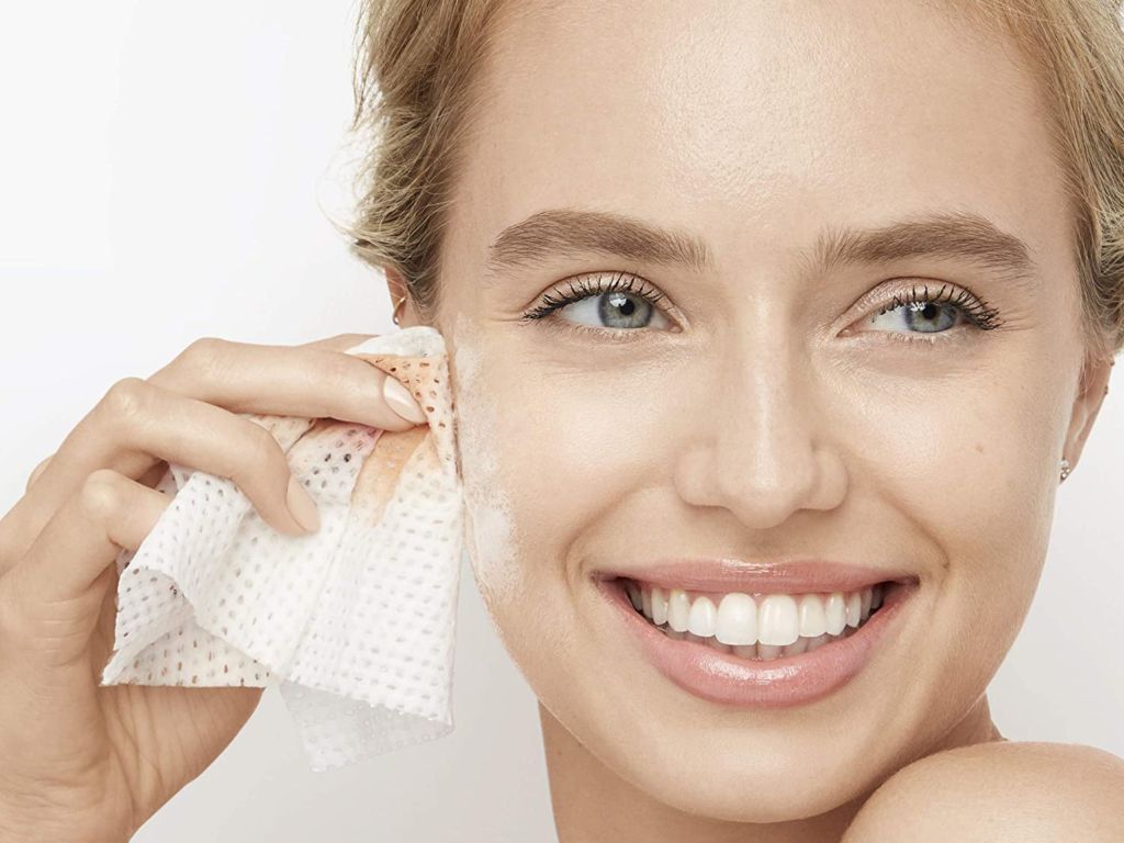 A woman uses a facial wipe on her cheek.