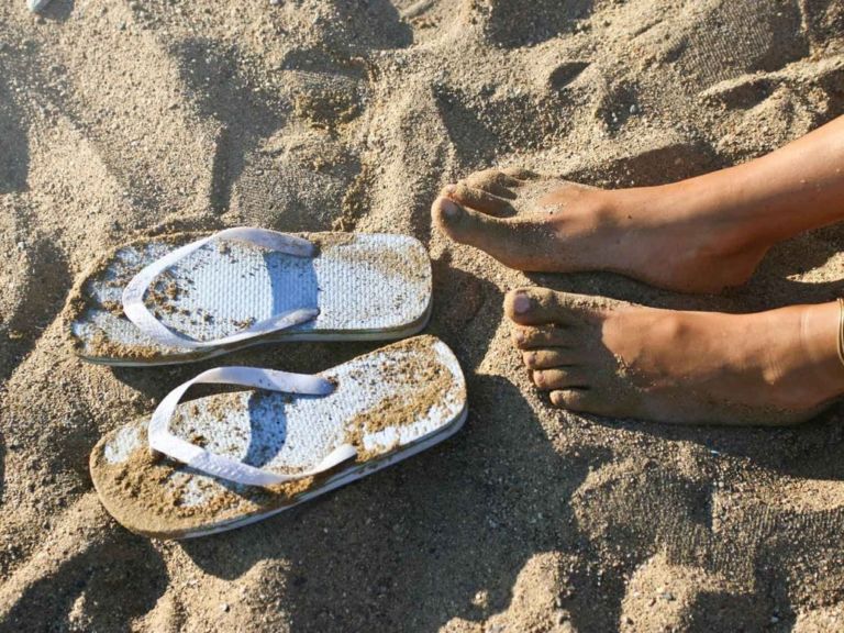 Bare feet on a sandy beach with flip flops