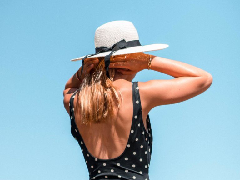 Woman in black and white bathing suit wearing a sun hat