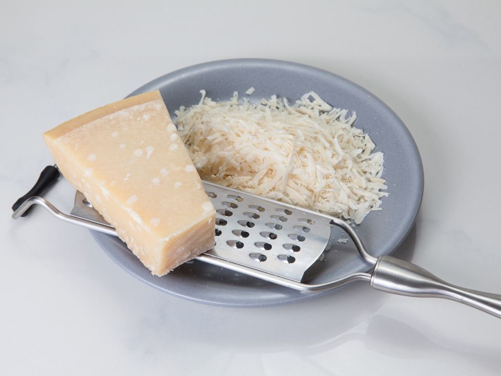 A cheese grater next to shredded cheese