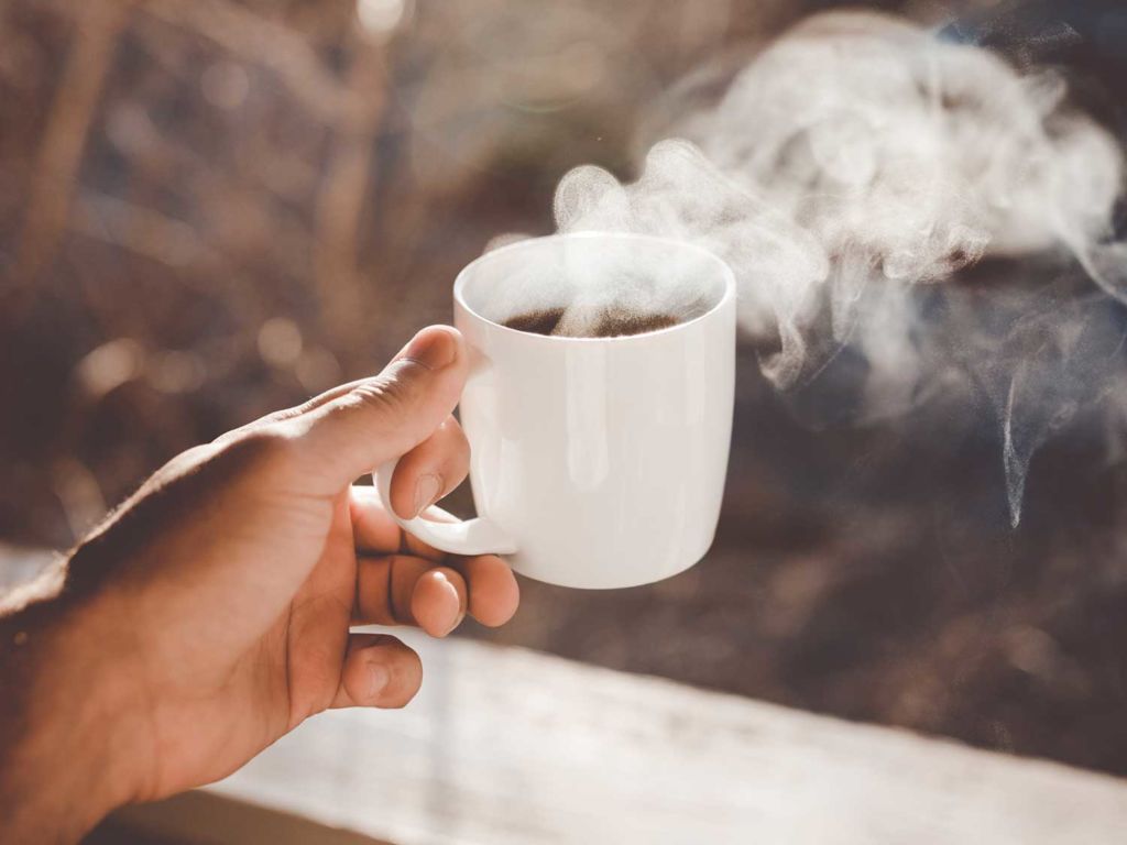 Man holding a steaming cup of coffee.