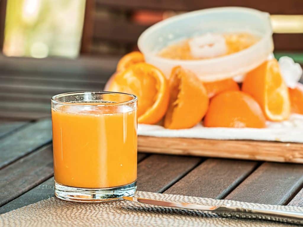 Orange juice in a glass next to sliced oranges.
