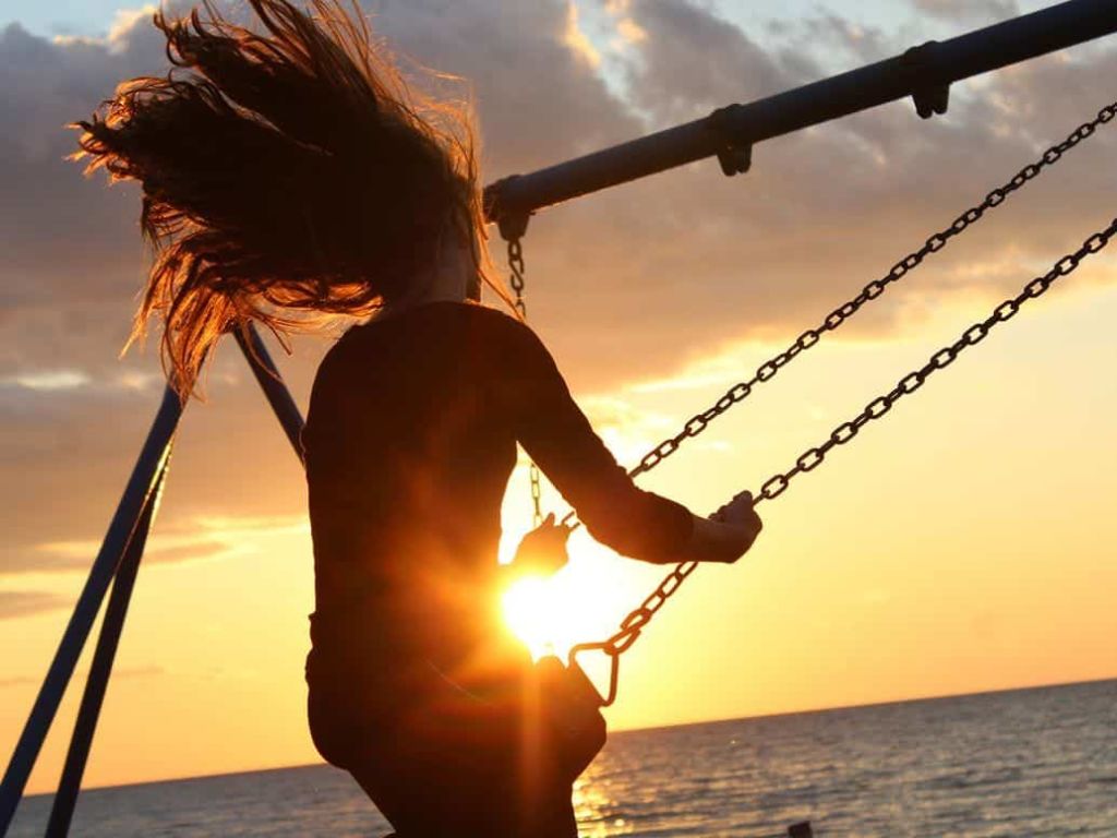 Woman on a swing set in the sunset.